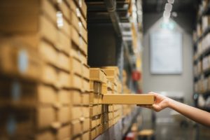 "Cardboard box package with blur hand of shopper woman picking product from shelf in warehouse. Premium Photo"